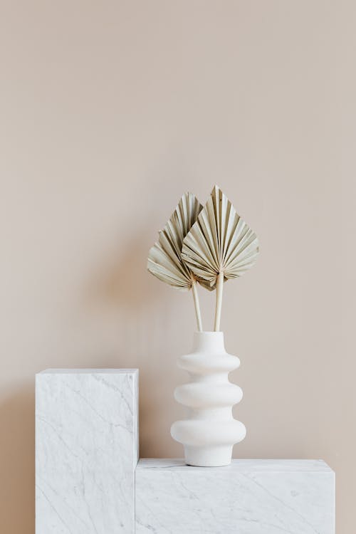 Free Decorative golden leaves in unique formed white vase placed on marble table against beige background Stock Photo