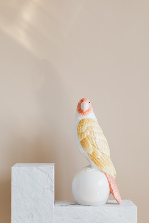 White marble patterned stand with glazed ceramic figurine in shape of parrot on white ball