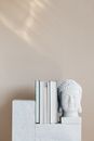 Set of various books composed with white Buddha head statuette on marble stand against beige wall