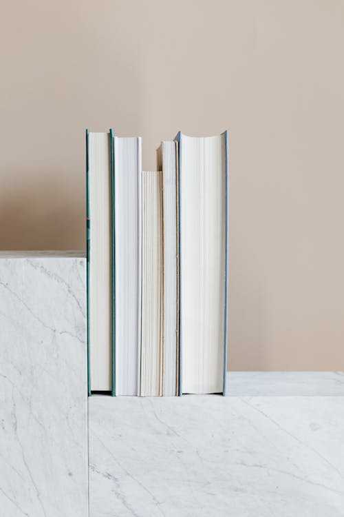 Set of various books placed on white marble patterned shelf against beige wall