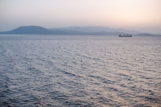 日落时分，平静的海面上，一艘货船以远山为背景