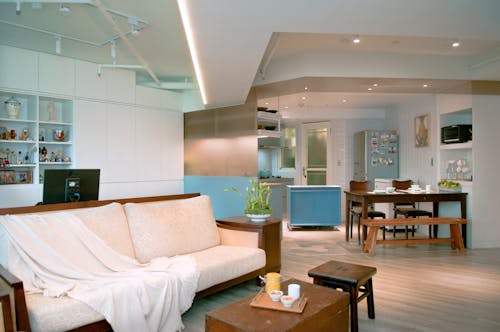 Interior of bright room with table and fridge in kitchen area and sofa in lounge zone decorated in white colors