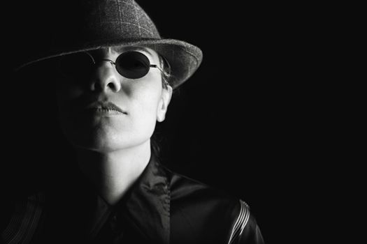 Black and white portrait of a person wearing sunglasses and a hat, exuding mystery.
