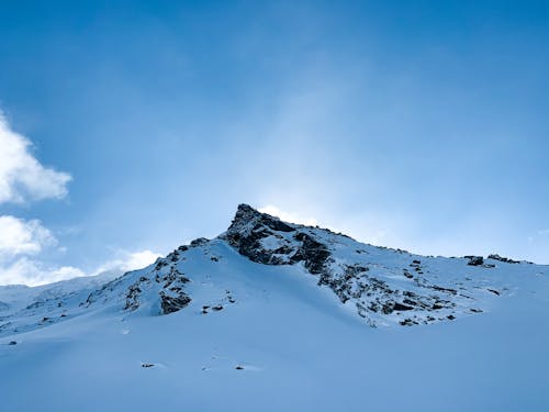 Light blue sky with clouds above mountain slope covered with snow in valley in wintertime