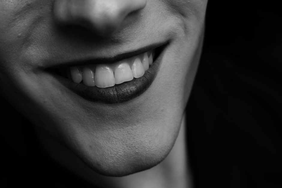 Black and white of unrecognizable person with dark lips and white even teeth smiling on black background