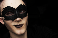 Young handsome male with cheekbones in black venetian carnival mask looking away with half smile