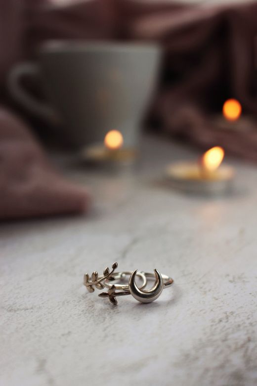 A silver ring with a crescent moon and leaf design resting on a table beside candlelight