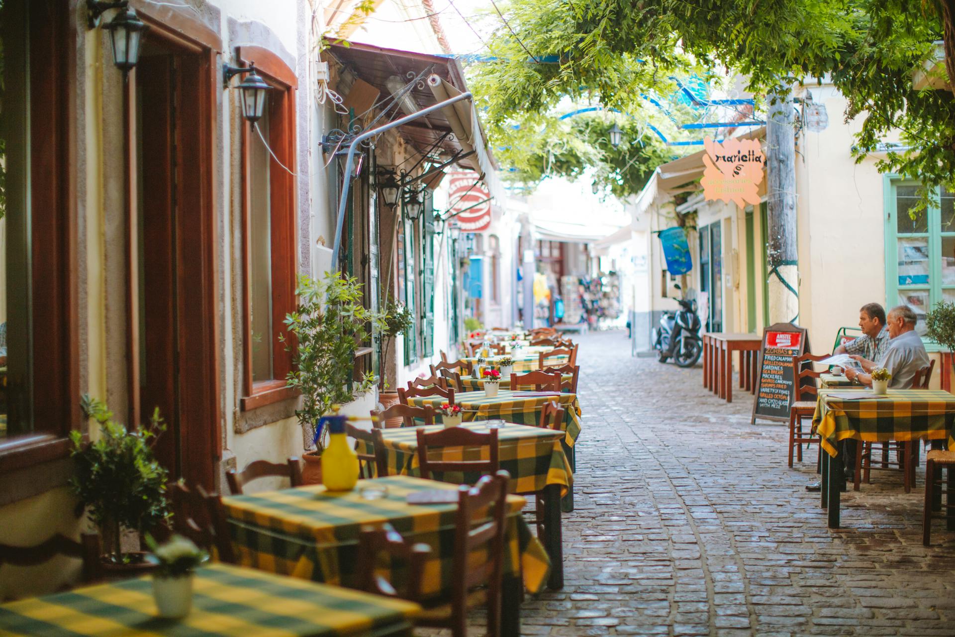 Charming outdoor café with checkered tablecloths lining a cobblestone street in a quaint European town.