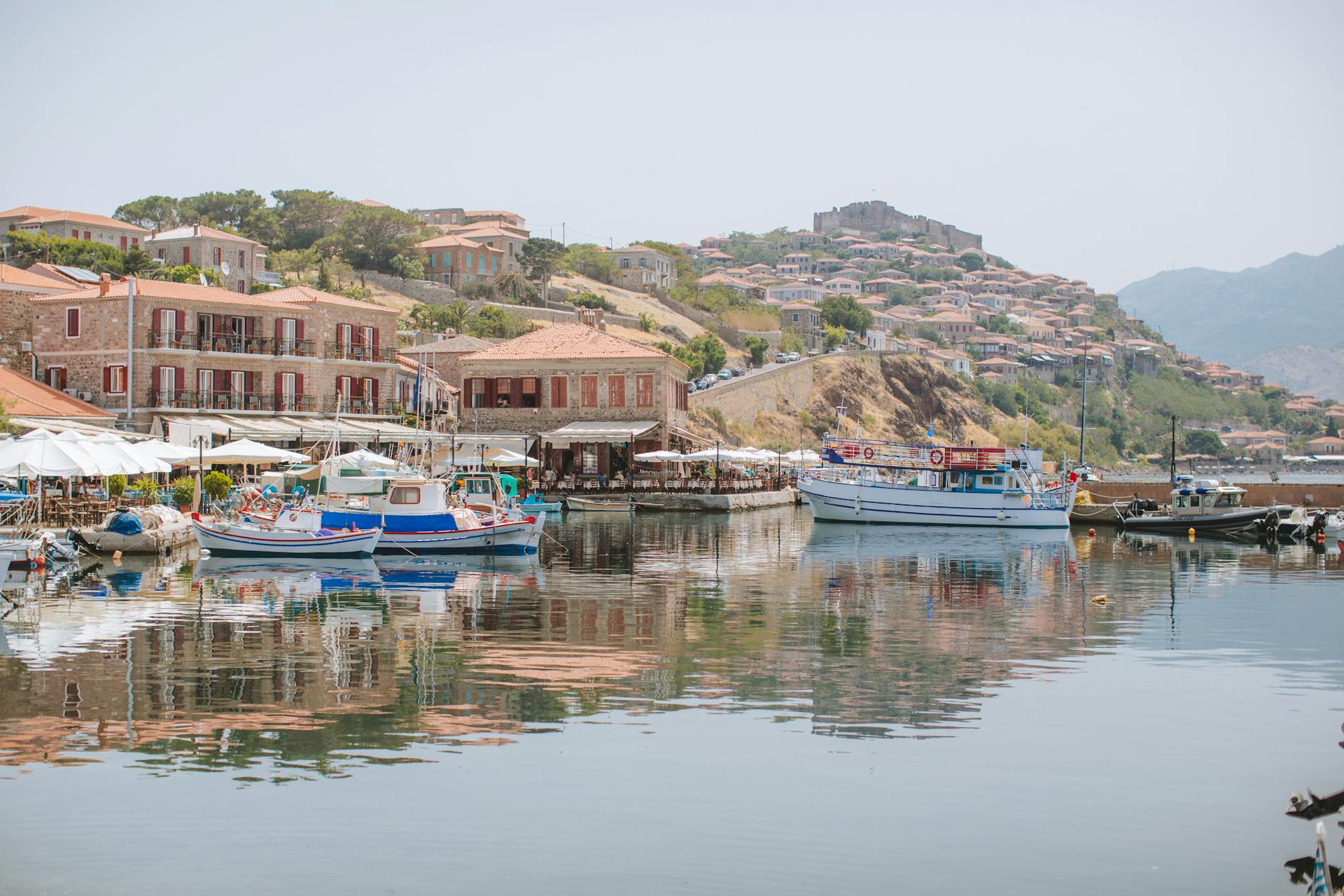 Scenic Greek harbor with boats and traditional architecture reflecting on the tranquil water.