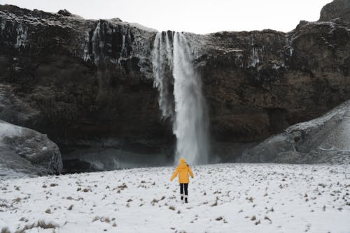 Free Person in Red Jacket Standing on White Snow Covered Ground Near Waterfalls Stock Photo