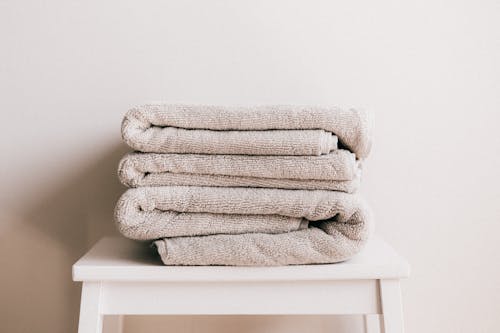 Stack of soft clean light beige folded towels placed on white minimalist stool against beige wall in daylight