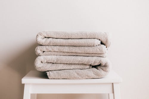 Free Stack of soft clean light beige folded towels placed on white minimalist stool against beige wall in daylight Stock Photo