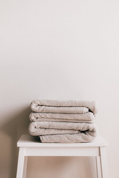 Minimalist composition of white simple stool with clean fresh folded gray towels against beige wall in bathroom