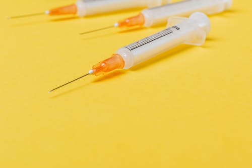 Free Medical single use disposable syringe without protective cover on needle and with empty barrel placed on bright yellow surface Stock Photo