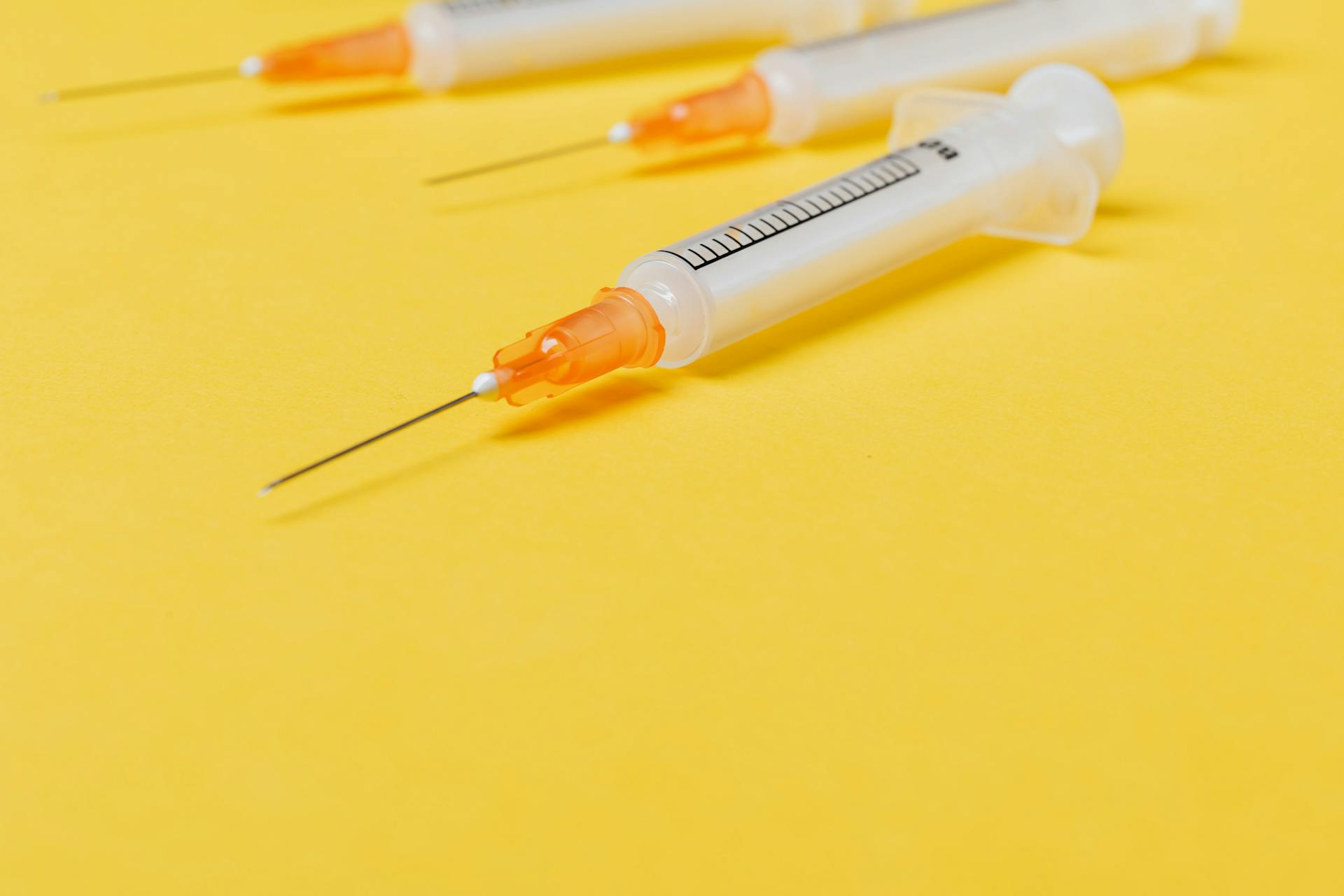 Medical single use disposable syringe without protective cover on needle and with empty barrel placed on bright yellow surface