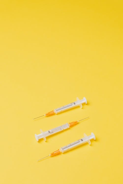 Free From above of plastic medical empty syringes with yellow needle hub and empty barrels lying in different directions without needle cover on yellow background Stock Photo