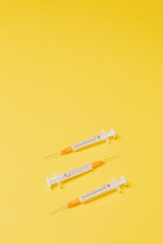 From above of plastic medical empty syringes with yellow needle hub and empty barrels lying in different directions without needle cover on yellow background