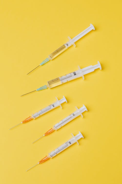 Free Top view arrangement of medical single use syringes with vaccine and small empty syringes without needle cover placed on yellow surface Stock Photo