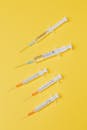 俯视黄色表面上放置着带有疫苗的一次性医用注射器和无针盖的小型空注射器