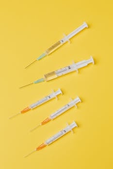 Top view arrangement of medical single use syringes with vaccine and small empty syringes without needle cover placed on yellow surface