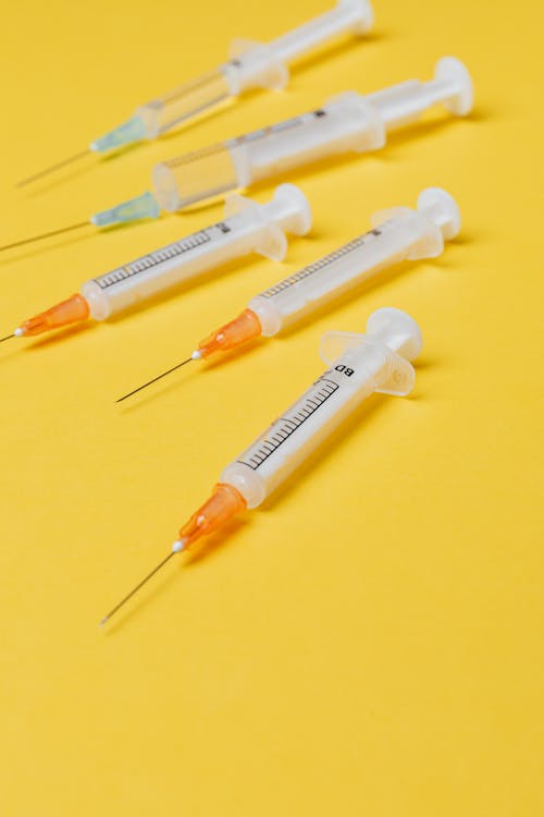 Plastic single use syringe injectors of different sizes with dose of vaccine placed on bright yellow surface without needle protective cover