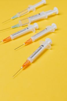 亮黄色表面上摆放着不同尺寸的一次性塑料注射器，里面装有疫苗剂量，没有针头保护罩