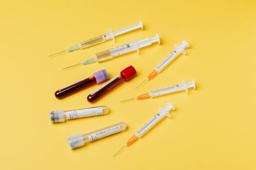 Free From above composition with medical syringes of different sizes arranged with test tubes filled with blood samples placed on yellow surface Stock Photo