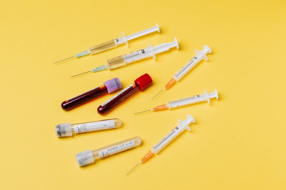 From above composition with medical syringes of different sizes arranged with test tubes filled with blood samples placed on yellow surface