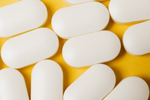 From above closeup of white ellipse shaped medical pills placed on bright yellow surface