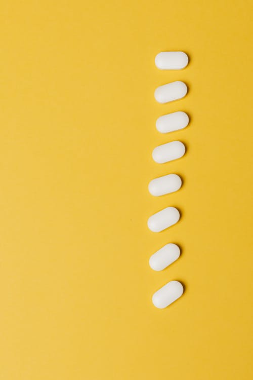 Top view composition of white medical pills placed in row vertically on vivid yellow background