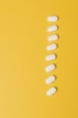 俯视图显示白色药丸垂直放置在鲜艳的黄色背景上