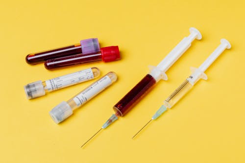 From above of medical syringe with medication near injector with blood sample arranged with filled clinical test tubes placed on yellow background