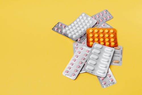 Heap of various pills in blisters on yellow background