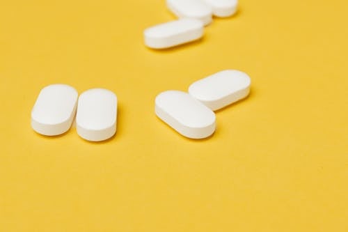 Set of medical white ellipse shaped pills placed in disorder on bright yellow background