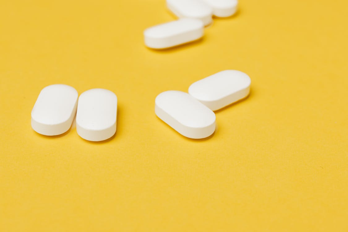 Heap of white pills on yellow surface