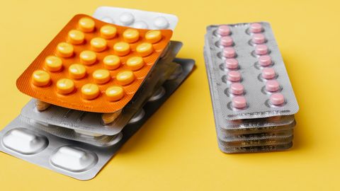 Heaps of various medication pills of different color and shape in blister packs placed on bright yellow background