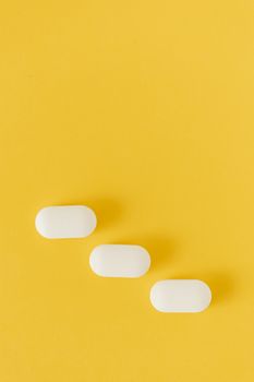 在黄色背景的下部，一颗白色椭圆形药丸斜躺在顶视图构图中
