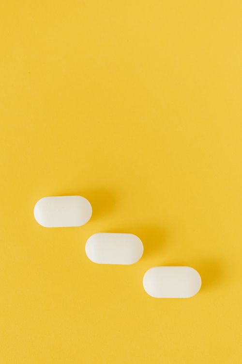 Free Top view composition with white ellipse shaped pills lying diagonally on lower part of yellow background Stock Photo