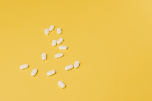 From above of small white ellipse shaped pills of same size randomly placed on bright yellow background