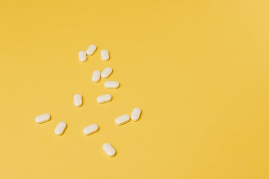 From above of small white ellipse shaped pills of same size randomly placed on bright yellow background