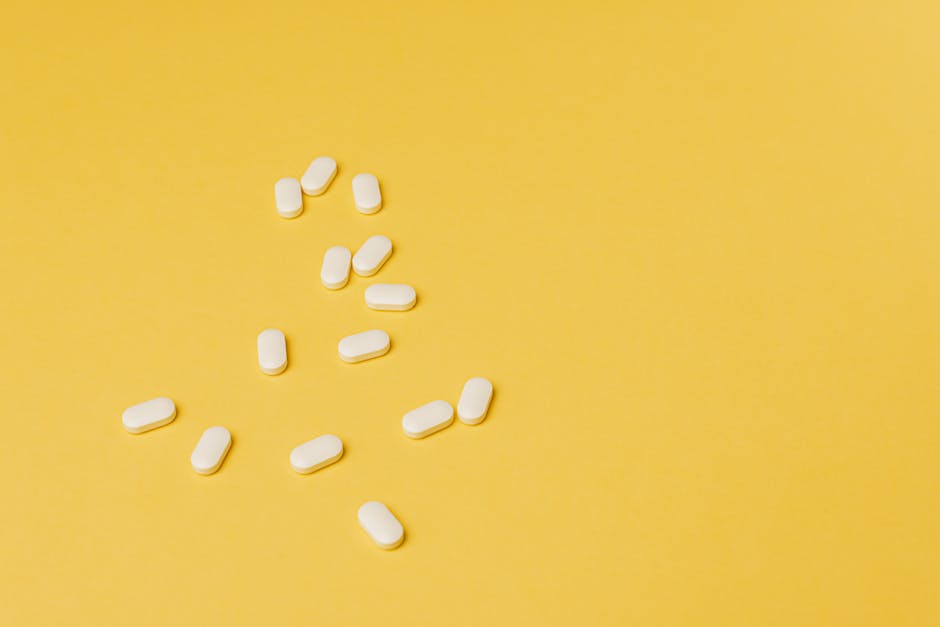 Da sopra, piccole pillole bianche a forma di ellisse dello stesso formato posizionate casualmente su uno sfondo giallo brillante