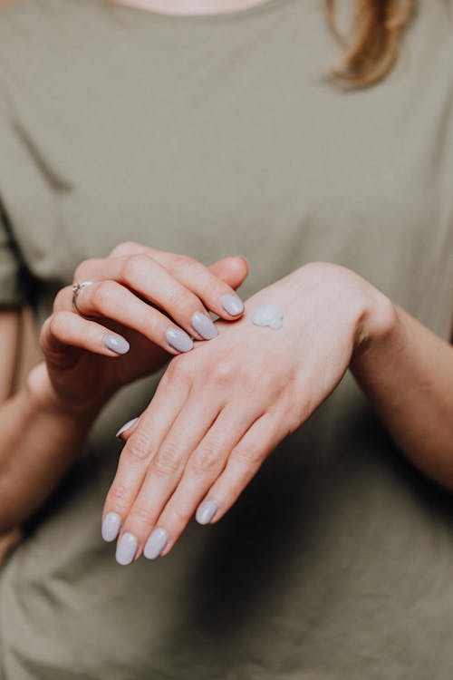 Crop anonymous female in casual outfit with stylish manicure and ring demonstrating small hand cream drop on back of hand