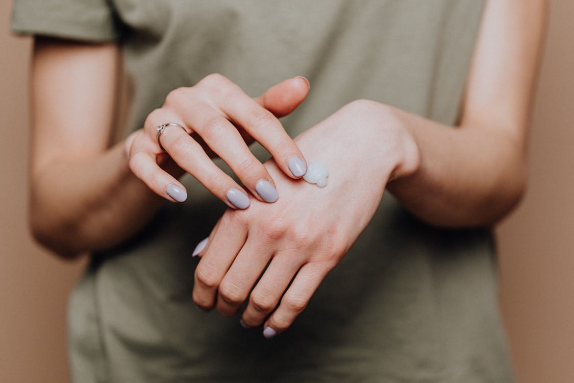 Free Crop anonymous female in casual shirt with manicured hands and ring softly rubbing hand moisturizer in back of hand skin Stock Photo