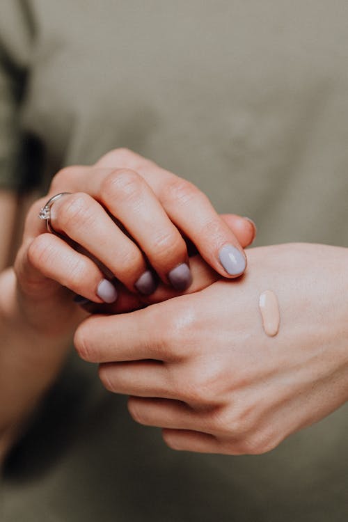 Free Crop unrecognizable female in casual clothes with manicured hands demonstrating drop of makeup foundartion on back of hand Stock Photo