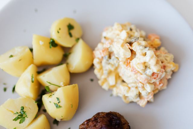 From above plate with boiled potatoes with parsley and portion of tasty nutritious Russian salad with boiled carrot potato and meat dressed with mayonnaise