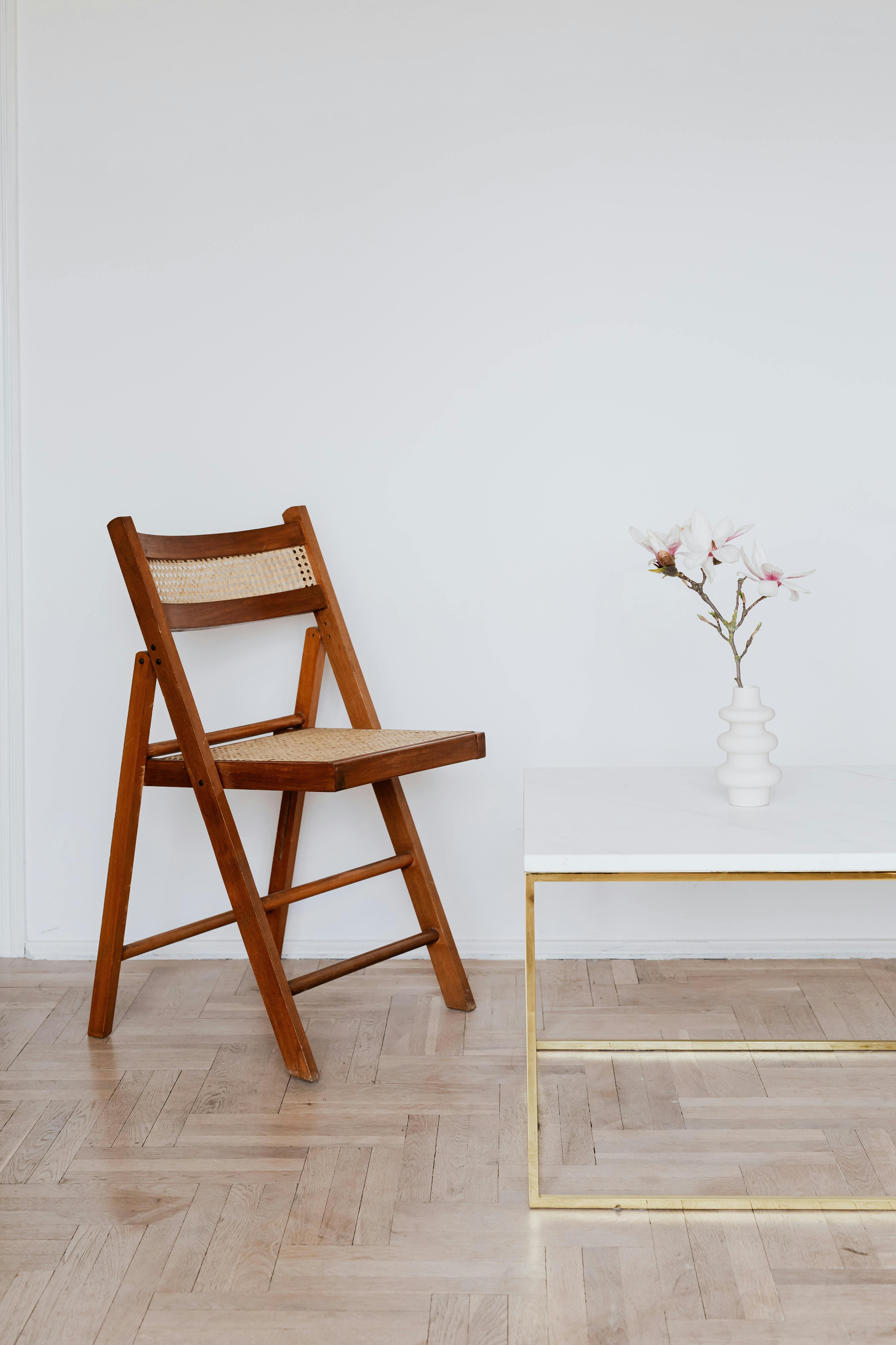 wooden chair near table with flower in white vase