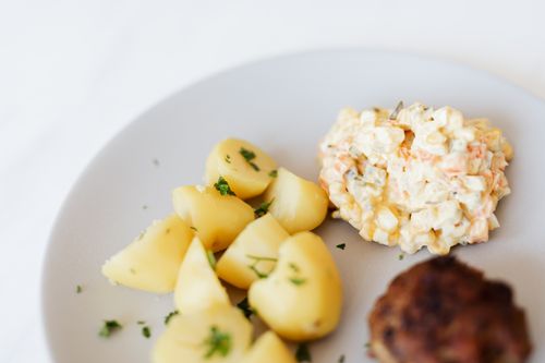 Free From above of plate with juicy fried meat cutlet served with delicious Russian meat salad and boiled potatoes topped with parsley placed on white table Stock Photo