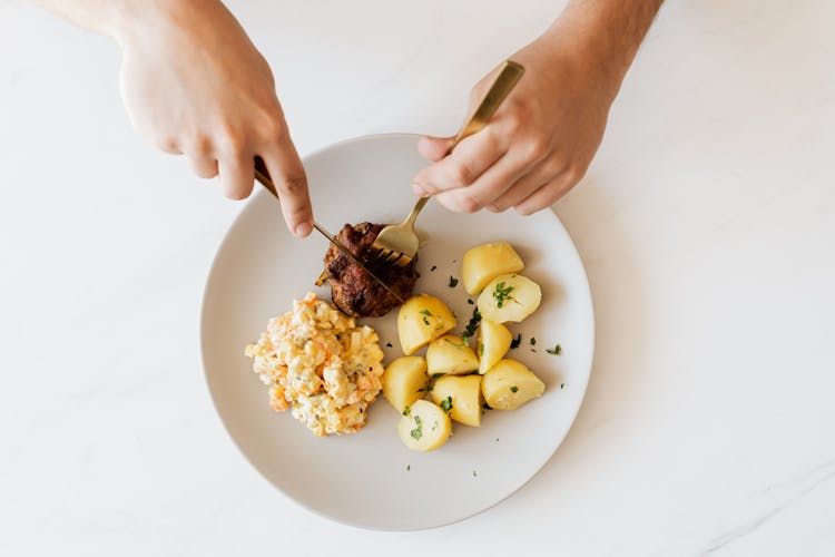 Crop Man Cutting Cutlet On Plate With Salad And Potatoes