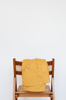 Minimalist photo of a mustard yellow jacket draped over a vintage wooden chair against a white background.