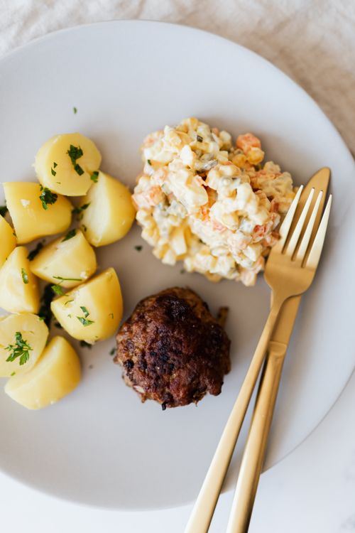 Free Top view of yummy potatoes and delicious meat rissole with vegetable and egg salad with cream served on white plate with gold plated fork and knife Stock Photo